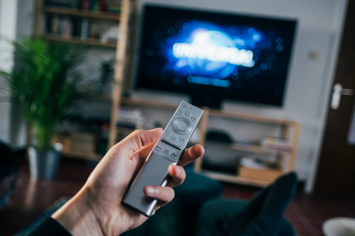 Hand holding a TV remote in front of a smart TV